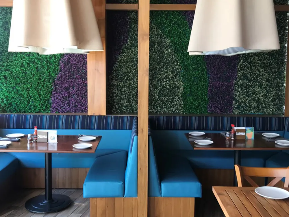 Muro verde artificial en el interior de un restaurante, detrás de mesas y sillones