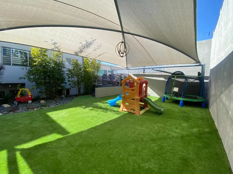 Área de juegos bajo toldo de sombra con pasto sintético