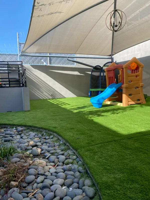 Área de juegos con pasto sintético, vela de sombra y borde de piedra de río