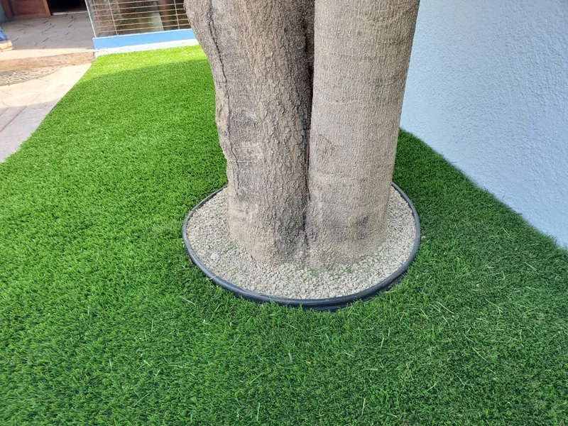Pasto sintético cortado alrededor del tronco de un árbol