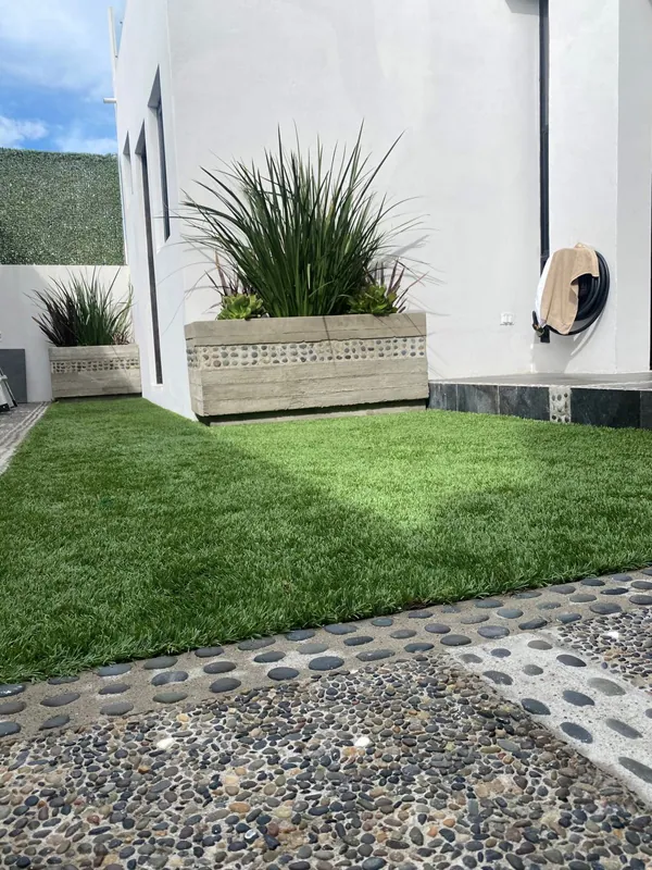 Franja de pasto sintético junto a grava y macetas en un patio estrecho