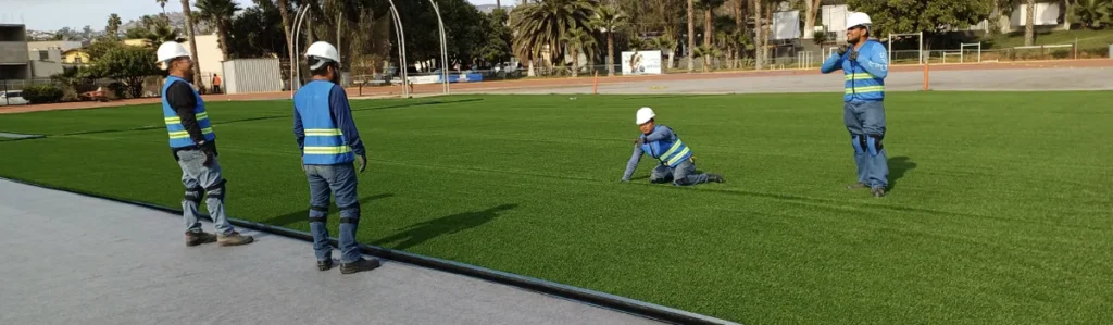 Equipo de instalación colocando pasto sintético en una cancha deportiva