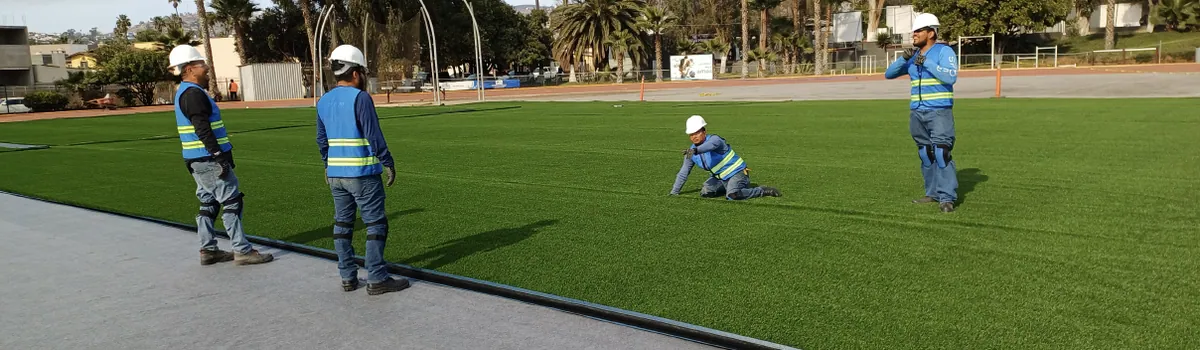 Equipo de instalación colocando pasto sintético en una cancha deportiva