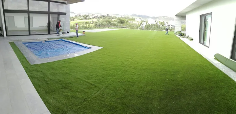 Jardín amplio con pasto sintético junto a una alberca