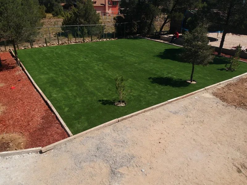 Jardín de pasto sintético delimitado con borde, rodeado de tierra y corteza