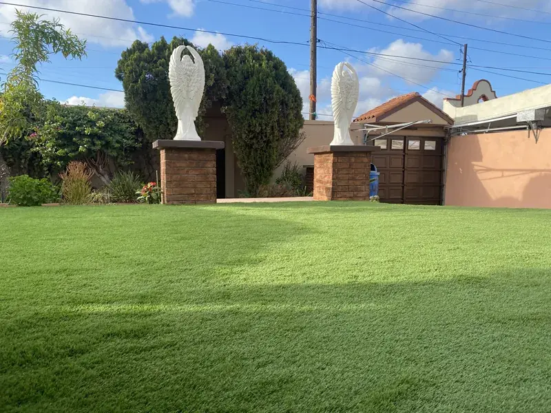 Jardín grande de pasto sintético a pleno sol, frente a una casa