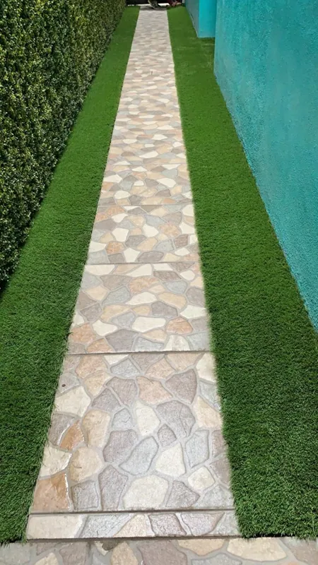 Pasillo angosto con camino de laja y pasto sintético a los lados