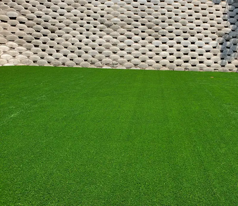 Pasto sintético parejo y con la fibra parada junto a un muro de block