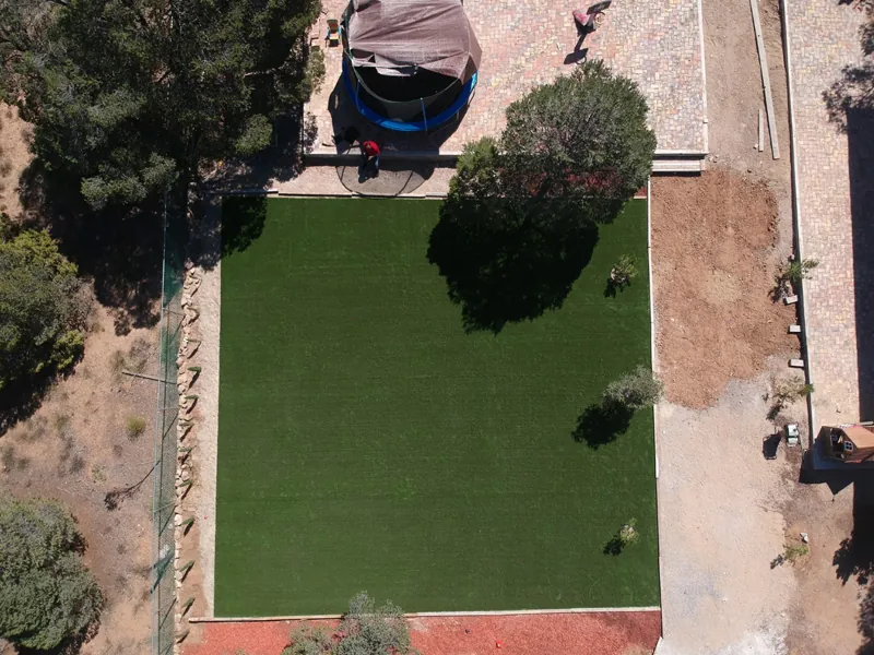 Vista aérea de un jardín de pasto sintético verde rodeado de terreno seco