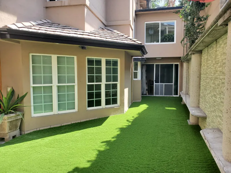 Patio angosto entre muros, con sombra, cubierto de pasto sintético