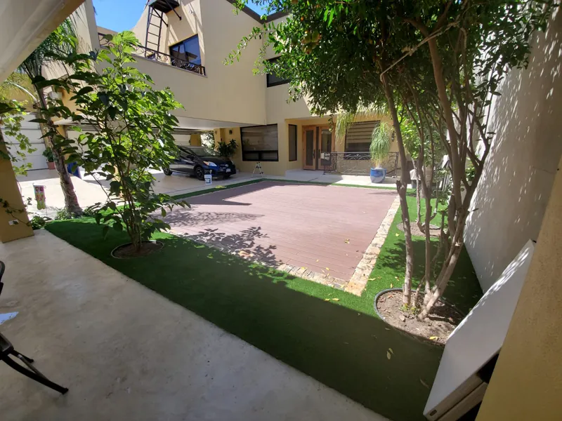 Patio con árboles y franja de pasto sintético junto al acceso de autos