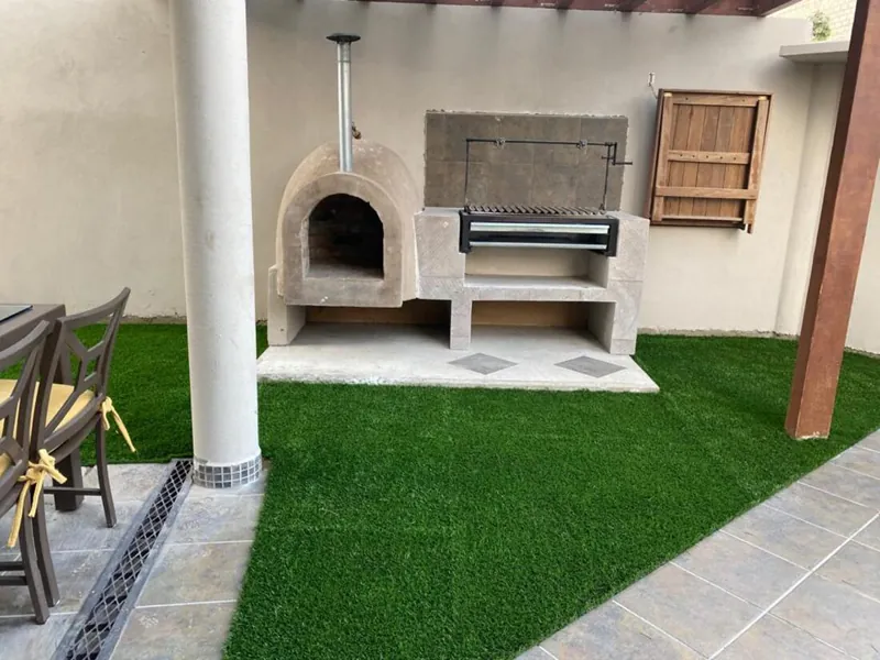 Patio con horno de leña y asador junto al pasto sintético