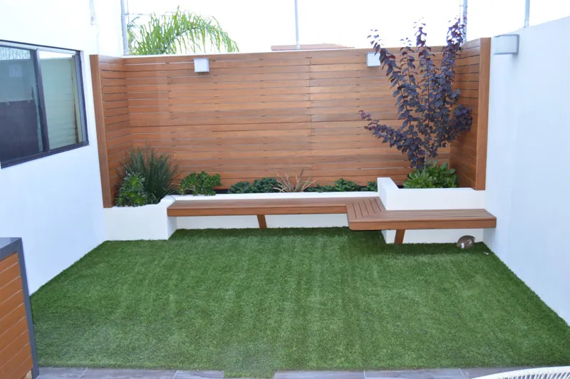 Patio pequeño con banca de madera, muro de duela y pasto sintético