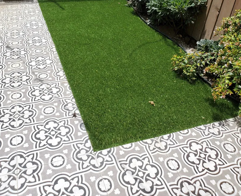 Remate recto de pasto sintético contra un piso de loseta decorada