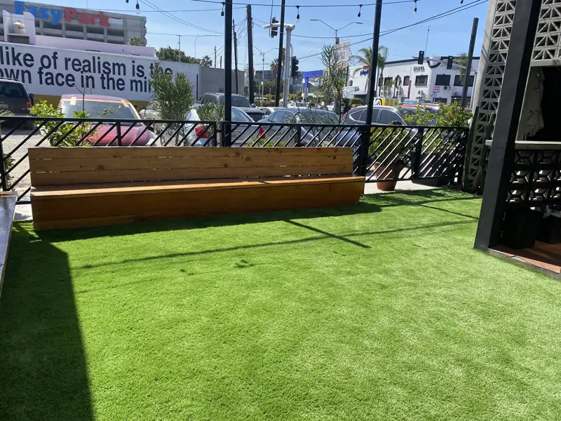 Terraza con banca de madera y pasto sintético junto a la calle