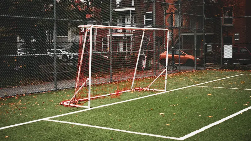 Portería de fútbol sobre pasto sintético en una cancha cercada con malla