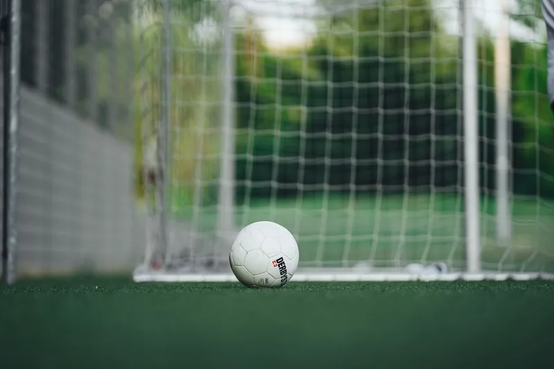 Balón dentro de una portería de fútbol sobre superficie verde