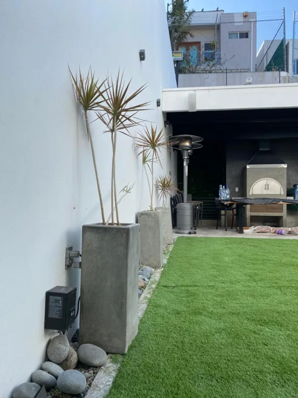 Remate de pasto sintético contra un muro blanco con borde de piedras
